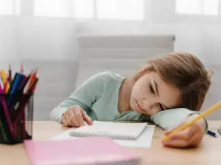 tired girl sat at desk doing homework